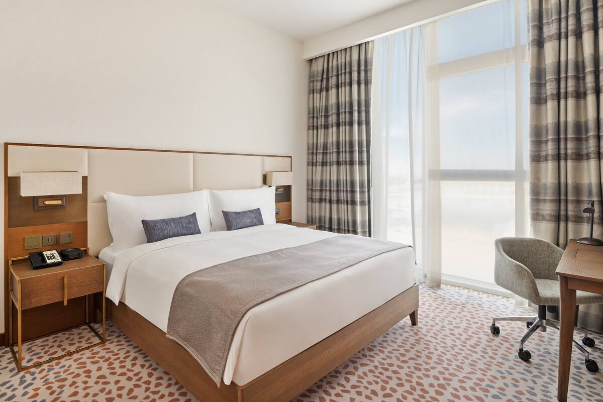 Une chambre d’hôtel avec un grand lit, un bureau, une chaise et une vue sur le ciel par la fenêtre.