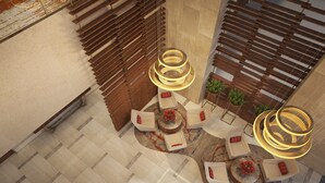 Un amplio vestíbulo con una zona de estar central, con mesas y sillas redondas, rodeado de listones de madera y un muro decorativo.