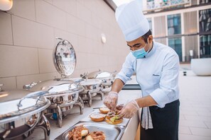 A chef preparing food outdoors with stainless steel equipment and a modern building in the background. - Staybridge Suites Dubai Al-Maktoum Airport by IHG (Dubai)