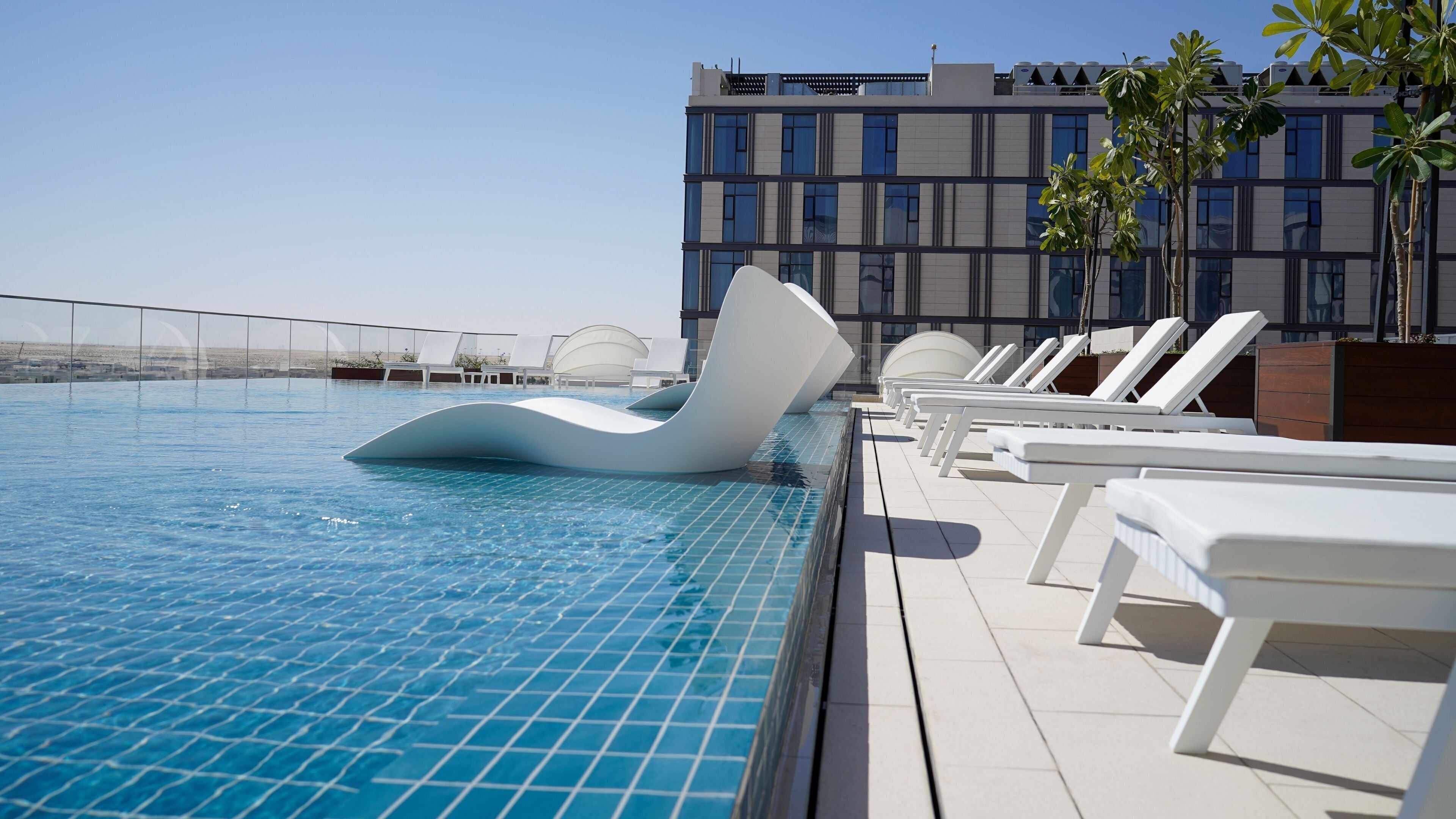 A swimming pool with modern sun loungers and a building in the background.