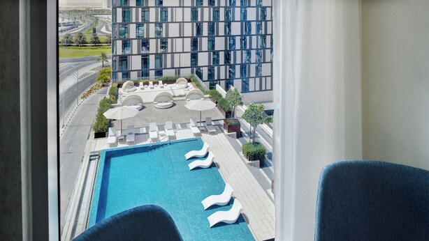 Una piscina en la azotea con sillas de descanso y sombrillas, rodeada por un edificio moderno con ventanales amplios.