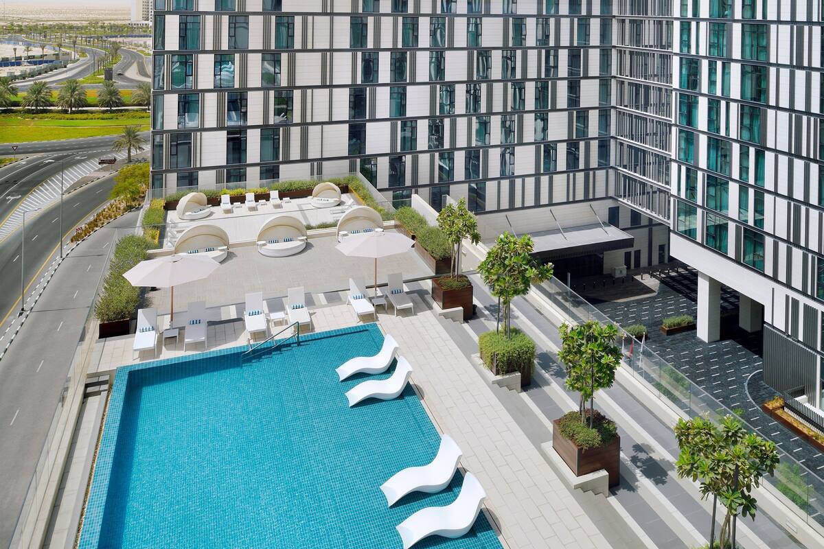 Un hôtel moderne doté d’une piscine sur le toit, de chaises longues et d’un jardin aménagé.