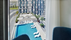 A rooftop pool with lounge chairs and umbrellas, surrounded by a modern building with large windows. - Holiday Inn Dubai Al-Maktoum Airport by IHG (Dubai)