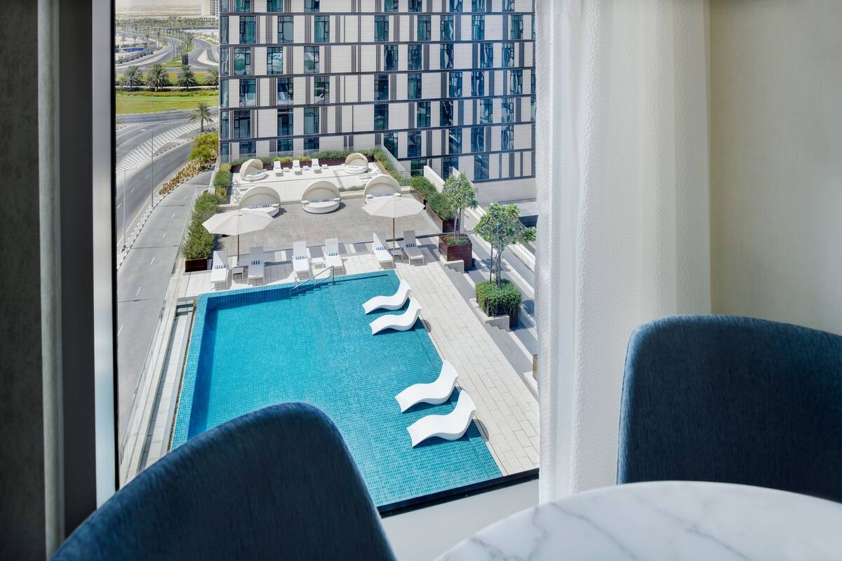 A rooftop pool with lounge chairs and umbrellas, surrounded by a modern building with large windows.