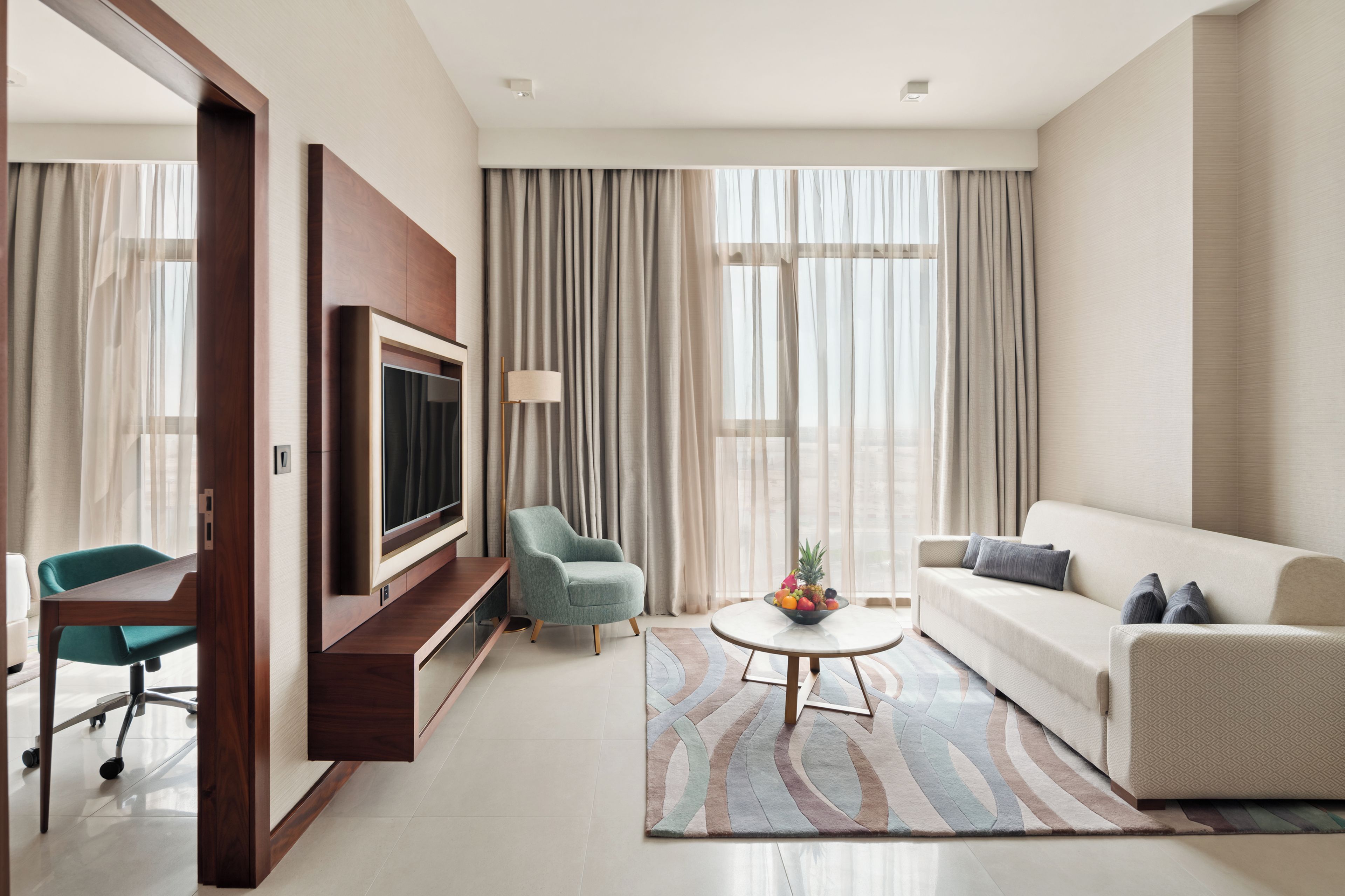 Un salon moderne avec un téléviseur à écran plat, un fauteuil turquoise, un canapé blanc et une table basse sur laquelle sont disposés des fruits.