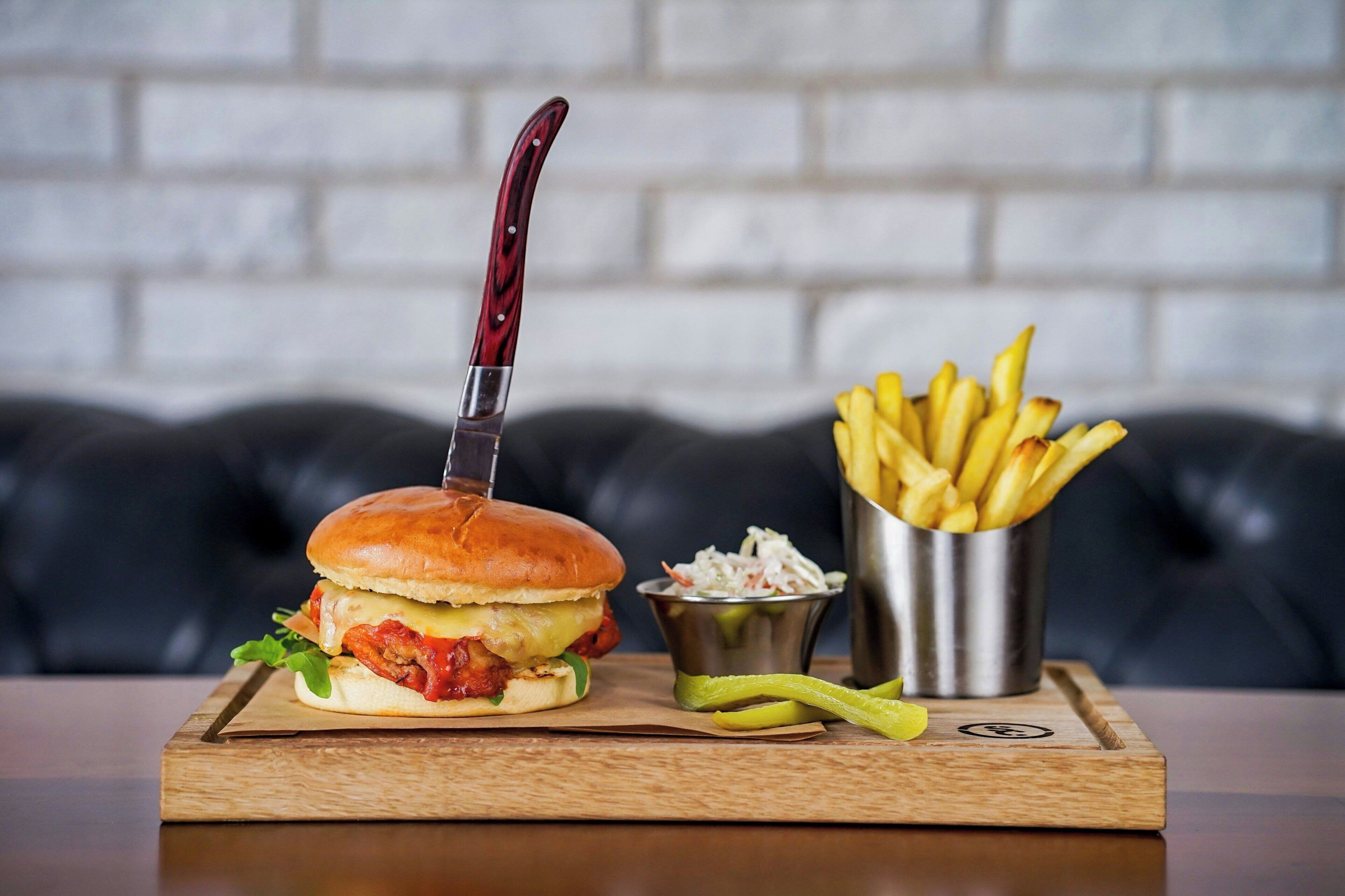 Una hamburguesa con cuchillo, papas fritas y ensalada de col sobre una tabla de madera.