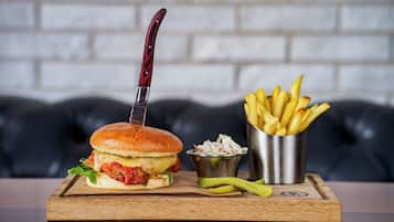 Una hamburguesa con cuchillo, papas fritas y ensalada de col sobre una tabla de madera.