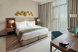 A hotel room with a bed, bedside tables with lamps, a desk with a telephone, and a view of the outdoors through large windows. - Holiday Inn Dubai Al-Maktoum Airport by IHG (Dubai)