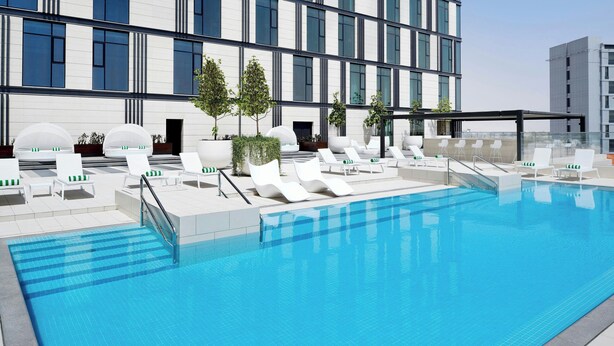 A modern hotel with a rooftop pool, white lounge chairs, and a clear view of the city skyline. - Holiday Inn Dubai Al-Maktoum Airport by IHG (Dubai)