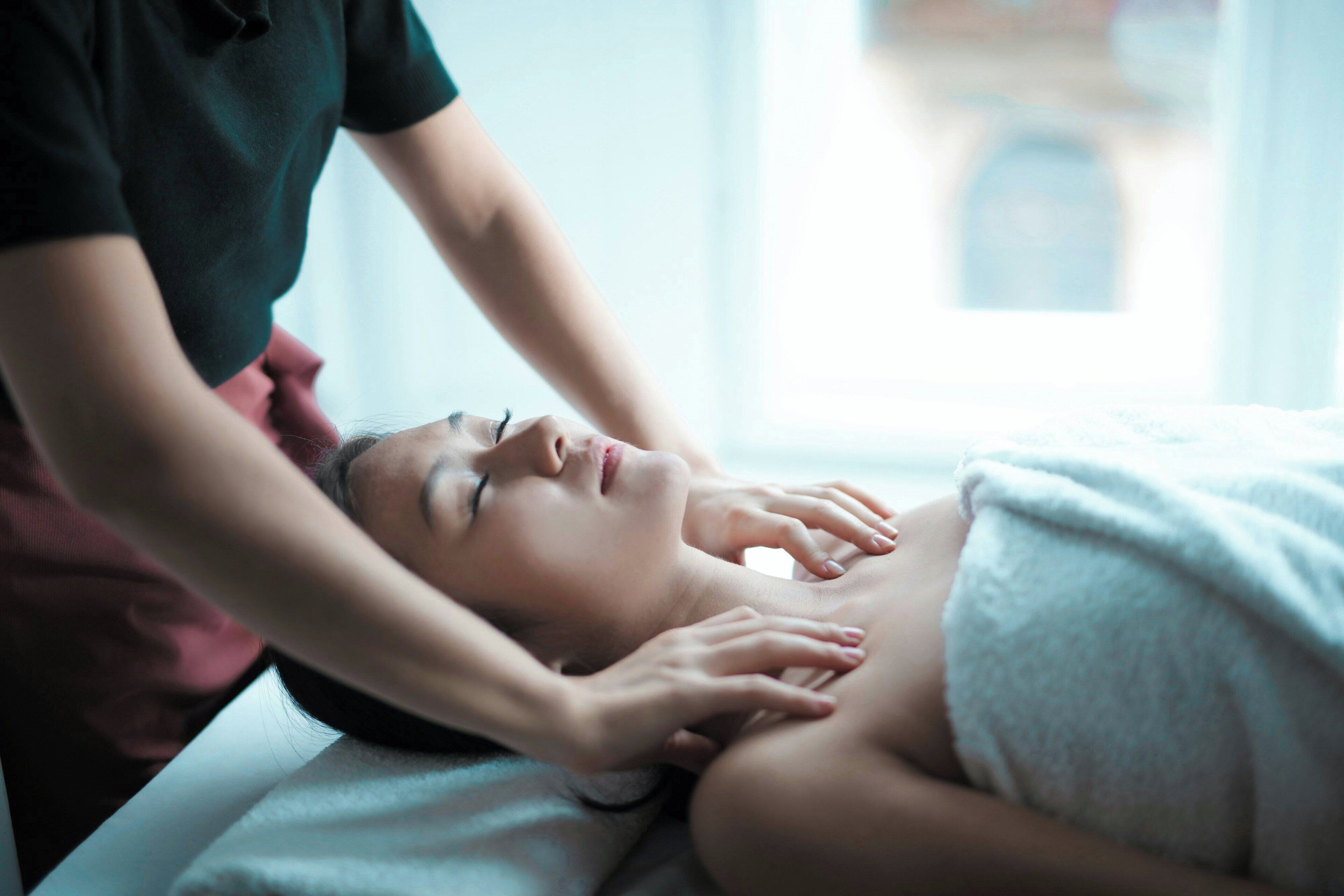 Een persoon ontvangt een massage in een ruimte met een raam en uitzicht op een gebouw.