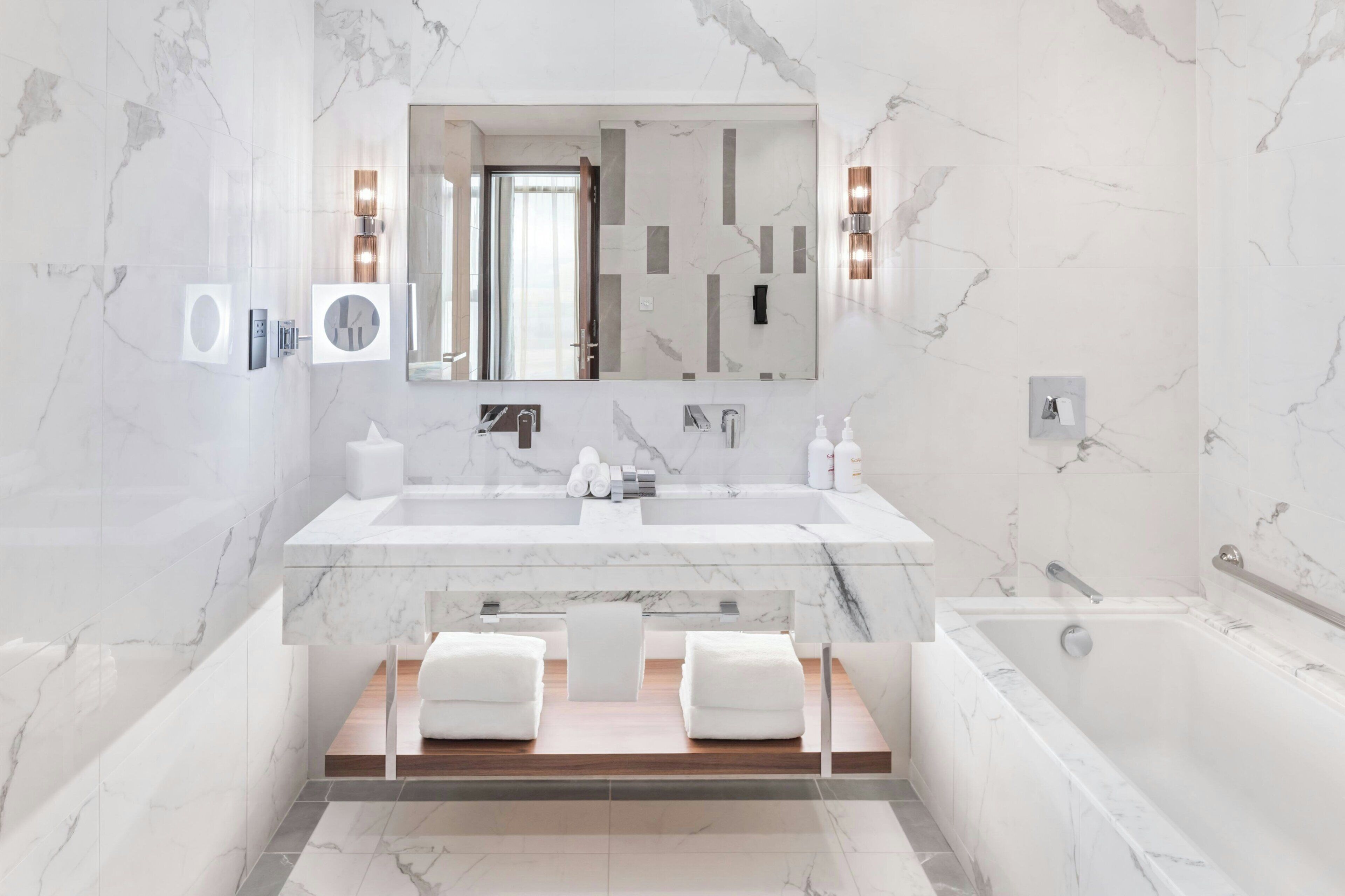 A modern bathroom with a large mirror, two sinks, a bathtub, and a toilet.
