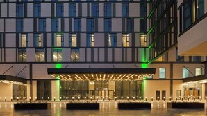 A modern hotel with a symmetrical facade, large windows, and a central entrance with a covered walkway. - Holiday Inn Dubai Al-Maktoum Airport by IHG (Dubai)