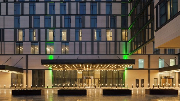 A modern hotel with a symmetrical facade, large windows, and a central entrance with a covered walkway. - Holiday Inn Dubai Al-Maktoum Airport by IHG (Dubai)