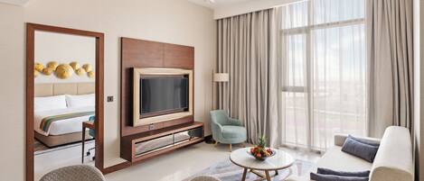 A modern hotel room with a bed, a television, a seating area with a coffee table, and a large window with curtains.