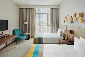 A hotel room with a bed, a desk, a chair, a TV, and a window with curtains.