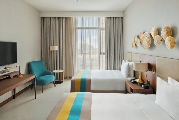 Une chambre d’hôtel avec un lit, un bureau, une chaise, une télévision et une fenêtre avec des rideaux.