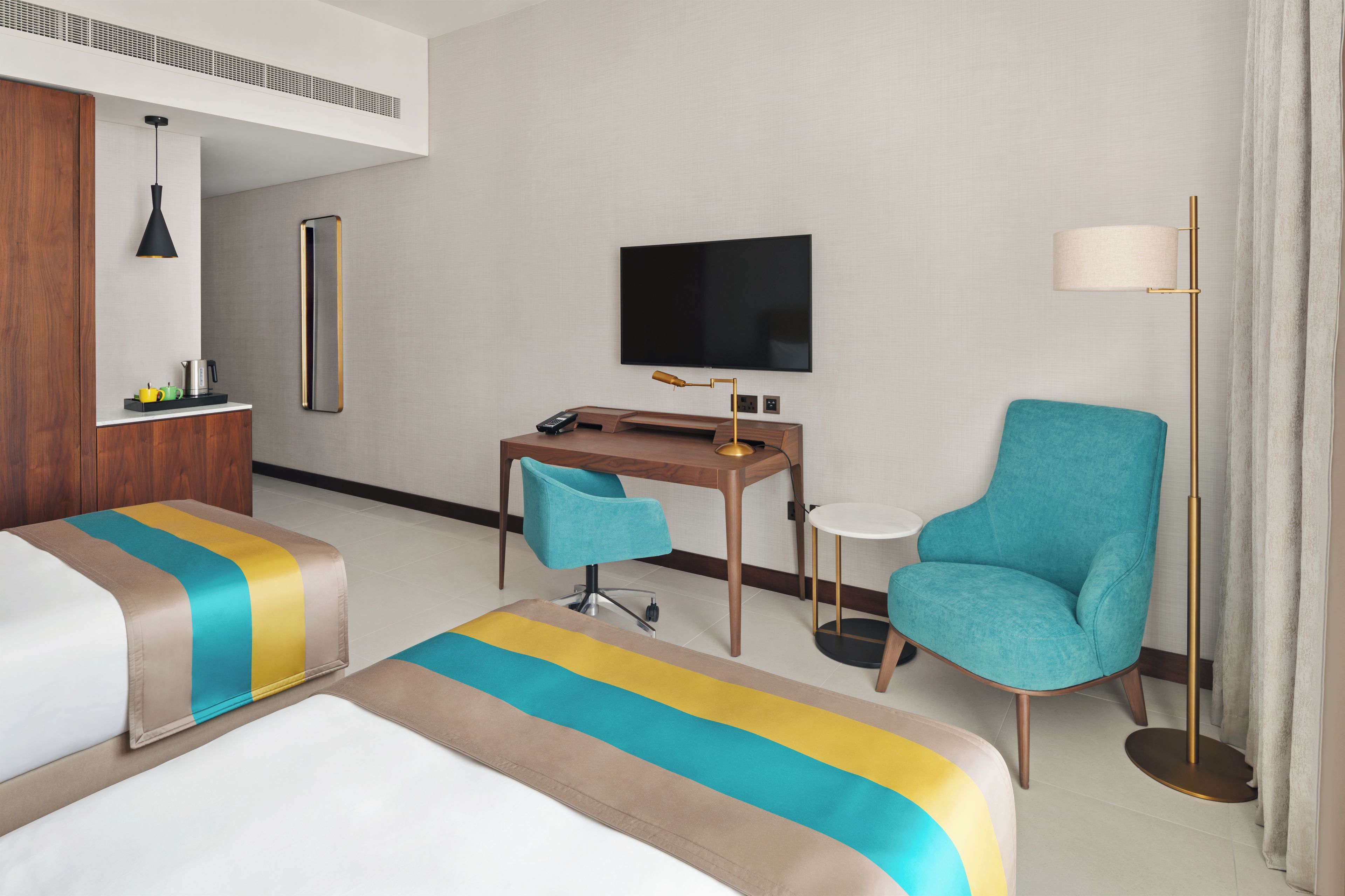 Una habitación de hotel con una cama, un escritorio, una silla, un televisor y una lámpara de pie.