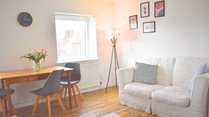 Un salon avec un canapé, une table à manger et des chaises, une lampe sur pied et une horloge au mur.