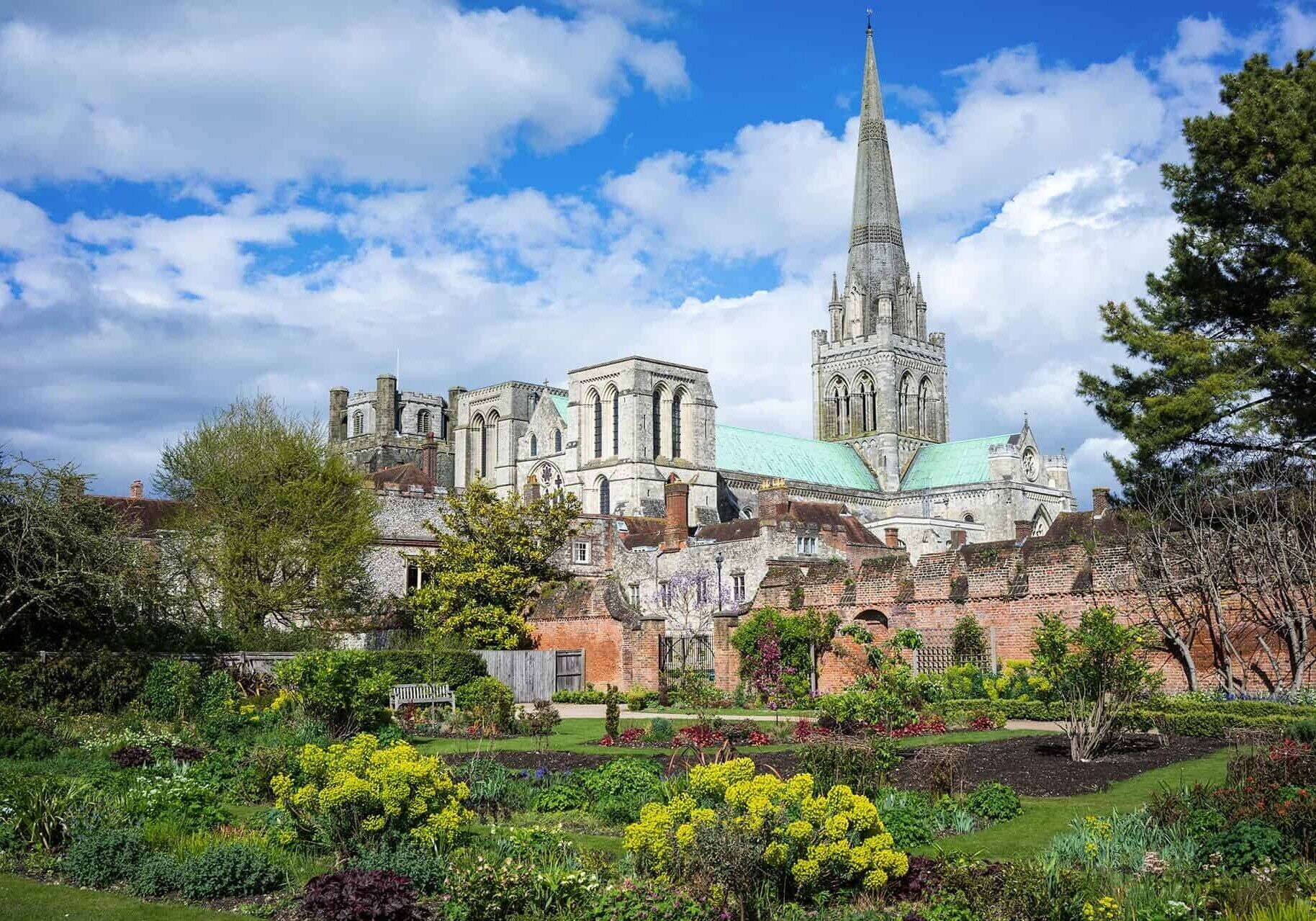 Una catedral histórica con una aguja alta, rodeada de un jardín bien cuidado con diversas plantas y flores.