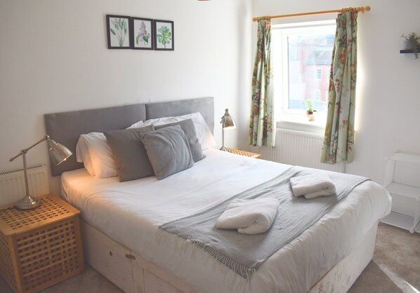 A neatly made bed with pillows, a bedside lamp, and a window with curtains.