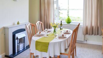 Een eetkamer met een ronde tafel gedekt voor vier personen, een open haard en uitzicht op de omgeving door grote ramen.