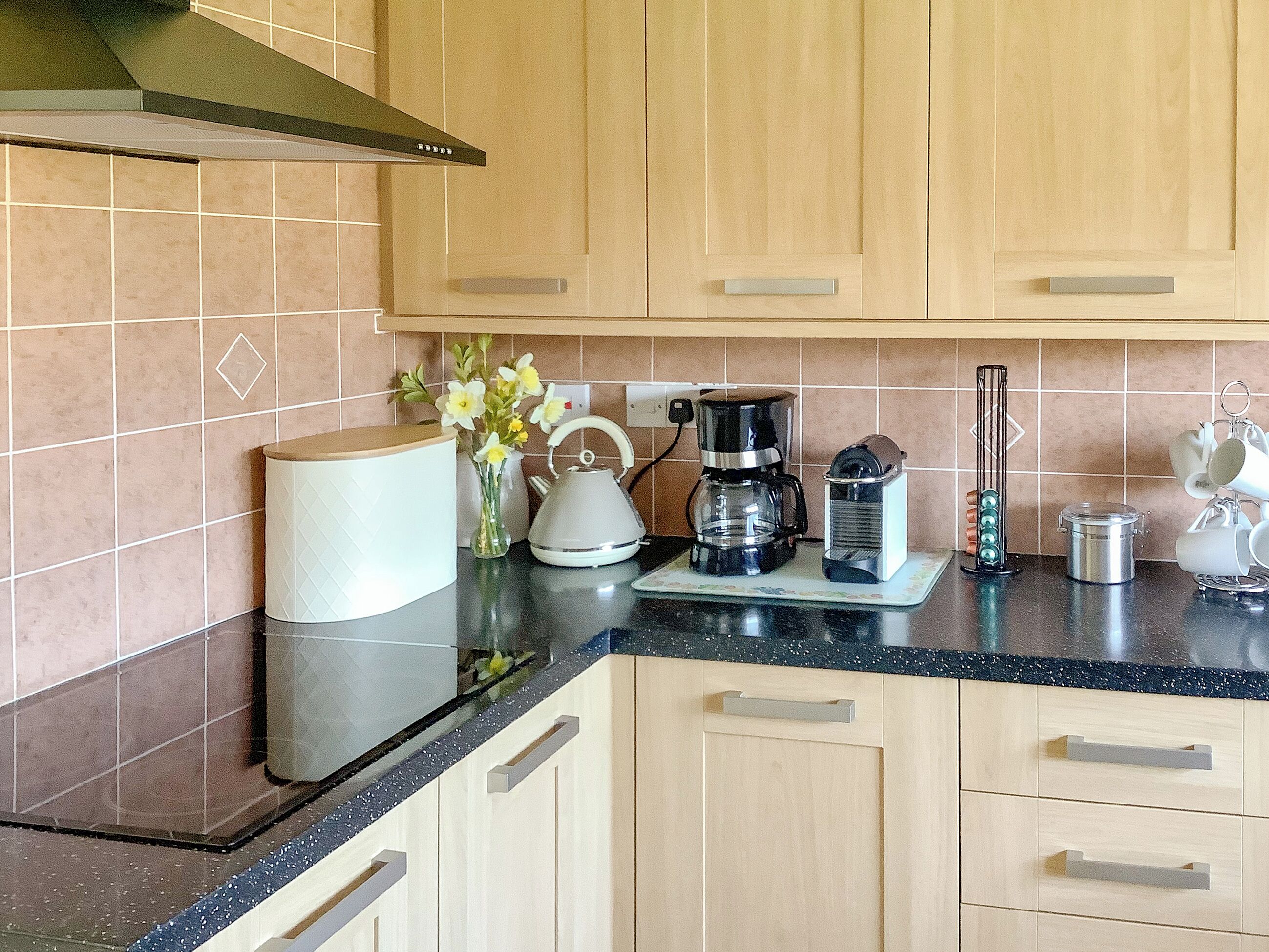 Een keuken met houten kastjes, een koffiezetapparaat, een waterkoker en een vaas met bloemen.