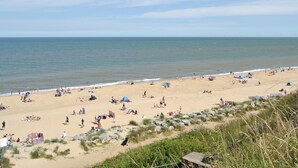 A beach with people sunbathing and swimming, tents, and a rocky area with vegetation. - The beach backed by sand dunes is just a short walk away. (California, near Great Yarmouth)