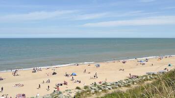 A beach with people sunbathing and swimming, tents, and a rocky area with vegetation.