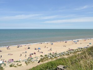 Een strand met mensen die zonnebaden en zwemmen, tenten, en een rotsachtig gebied met begroeiing.