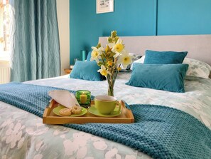 Een netjes opgemaakt bed met een bloemenbedekker, een dienblad met ontbijtartikelen, en een bloemenvaas op de hoofdeinde.