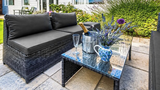 A black wicker sofa with cushions, a glass table with a vase of flowers, and a bottle of champagne. - The beach backed by sand dunes is just a short walk away. (California, near Great Yarmouth)