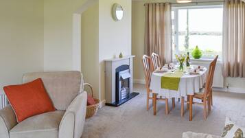 A living room with a fireplace, dining table set for four, and a sofa with a red pillow.