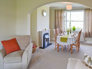 A living room with a fireplace, dining table set for four, and a sofa with a red pillow.