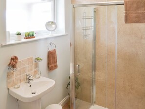 Een badkamer met een douchecabine van glas, een wastafel met spiegel en een raam boven de wastafel.
