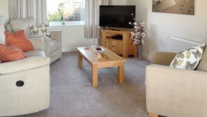 A living room with a sofa, coffee table, TV stand, and a window with curtains. - The beach backed by sand dunes is just a short walk away. (California, near Great Yarmouth)