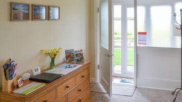 A reception area with a wooden desk, framed pictures on the wall, a vase with flowers, and a door leading outside.
