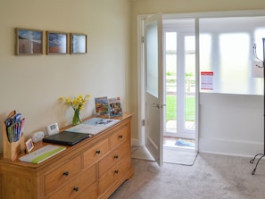 A reception area with a wooden desk, framed pictures on the wall, a vase with flowers, and a door leading outside.