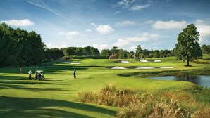 Een golfbaan met zandbunkers, een vijver en bomen.
