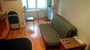 A small, sparsely furnished room with a sofa, a chair, a desk, and a standing heater.