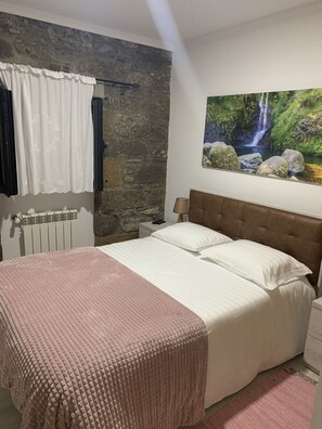 Ein Schlafzimmer mit Steinwand, einem Bett mit brauner Kopfteil, einem weißen Vorhang und einem Gemälde eines Wasserfalls.
