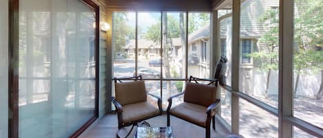 A sunroom with two chairs and a small table, large windows, and a view of a residential street.
