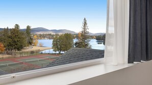 Vista desde una ventana que da a una cancha de tenis, con un lago y montañas al fondo.