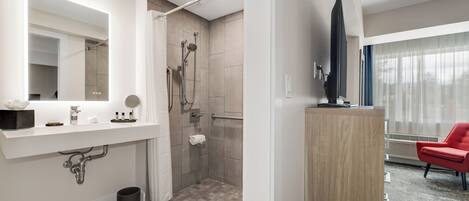 A modern bathroom with a large mirror, shower, and a red chair in the adjacent living area.