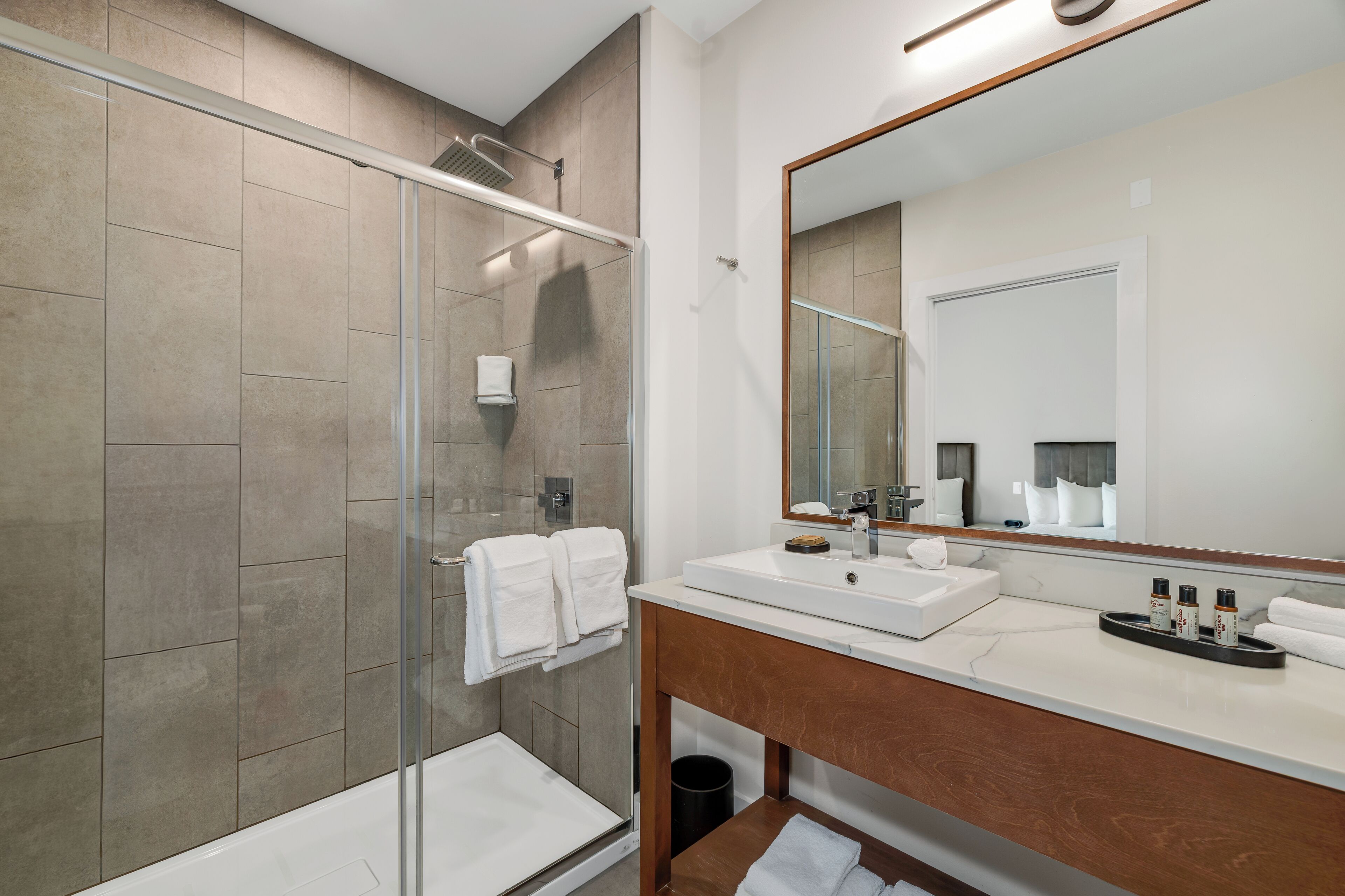 A modern bathroom with a glass-enclosed shower, a white sink, and a large mirror.
