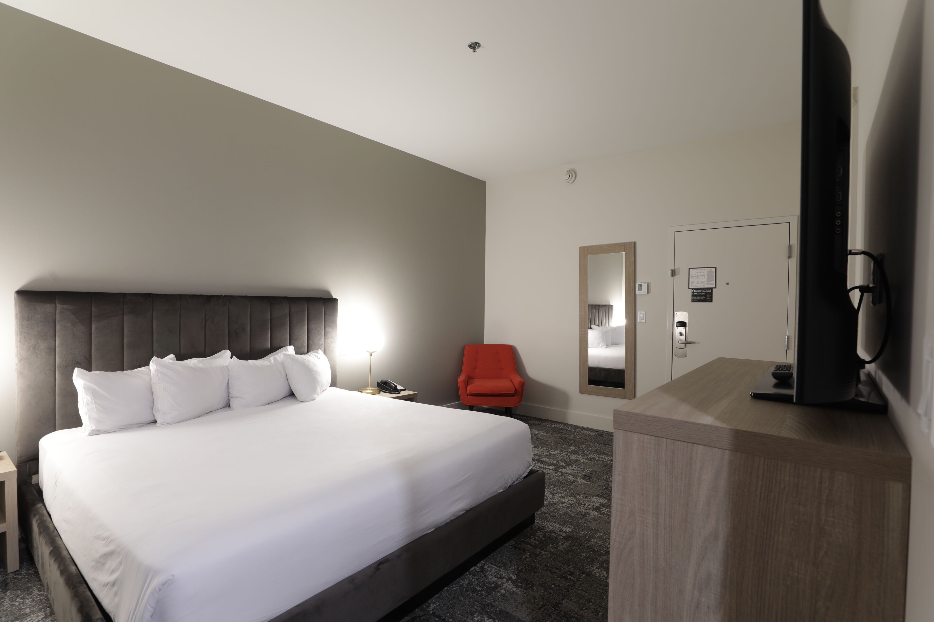 A hotel room with a large bed, a desk with a computer, a chair, a mirror, and a TV.