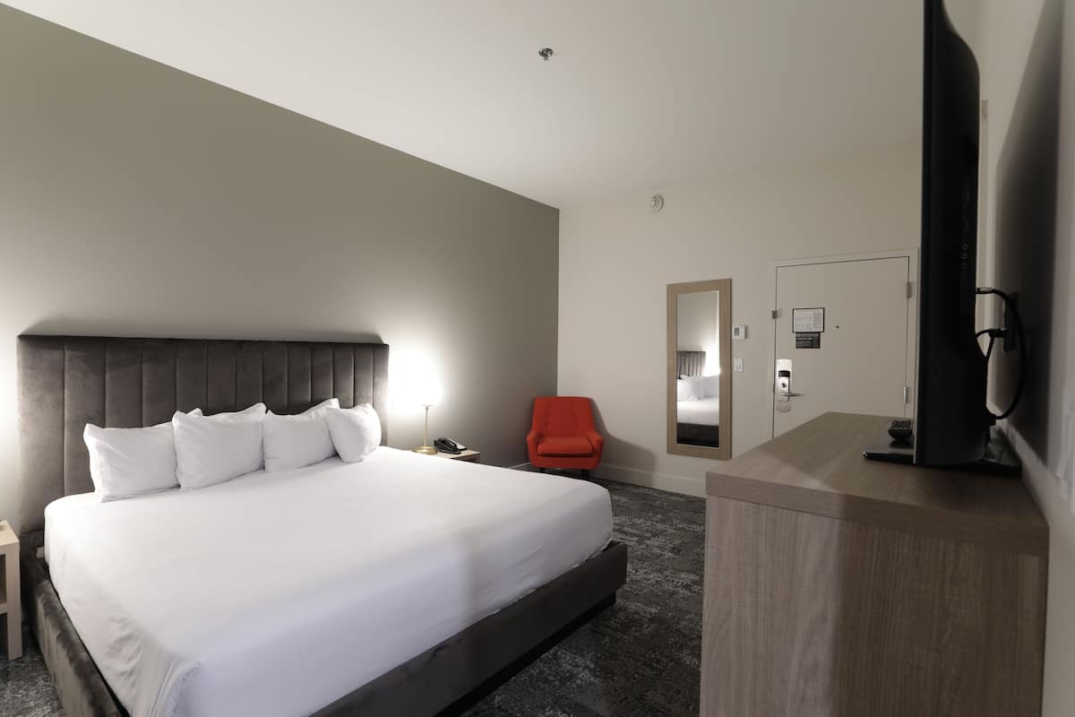 A hotel room with a large bed, a desk with a computer, a chair, a mirror, and a TV.