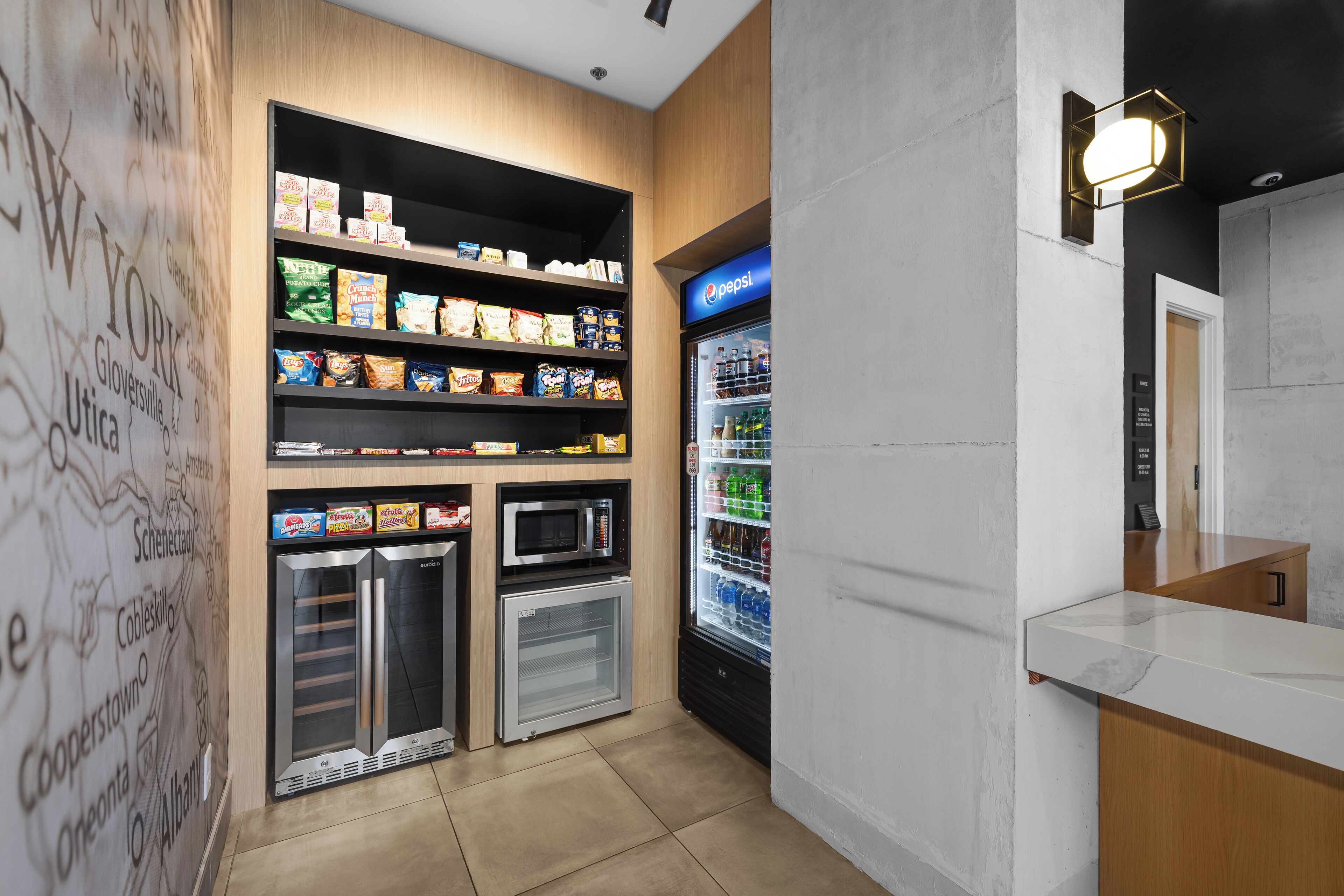 A kitchenette with a microwave, mini-fridge, and shelves stocked with snacks.