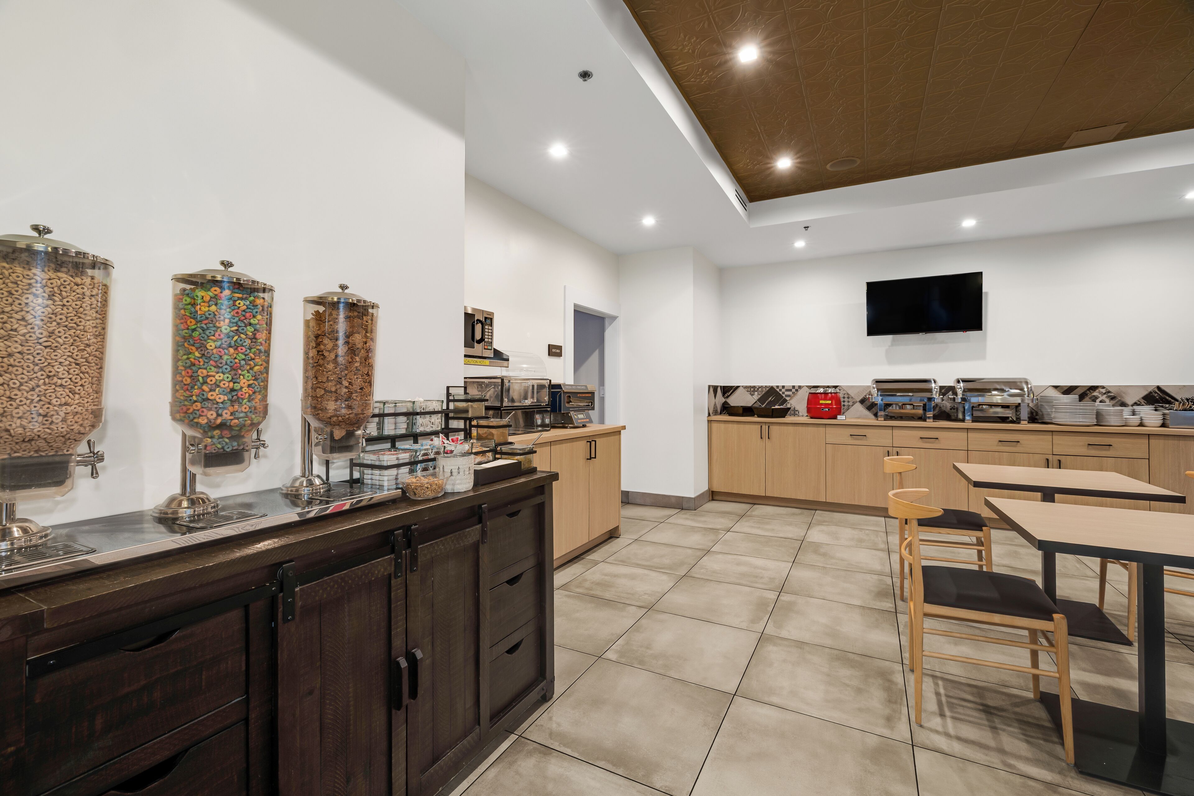 A modern kitchen with a breakfast bar, a TV mounted on the wall, and a coffee machine.