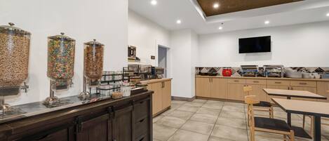 A modern kitchen with a breakfast bar, a TV mounted on the wall, and a coffee machine.