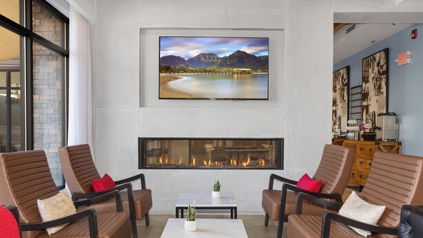 Un área de descanso moderna con sofás de cuero, un televisor de pantalla plana, una chimenea y vistas a un lago y montañas.